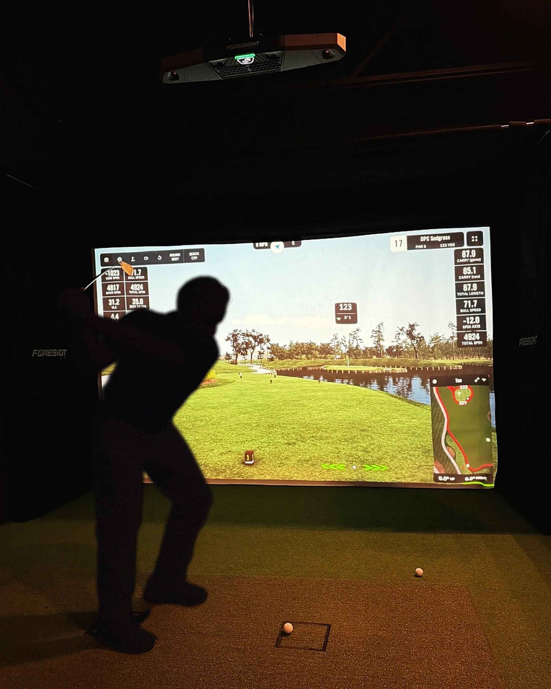A golfer mid-backswing in a private simulator bay at That Golf Place, silhouetted against the lit GSPro screen